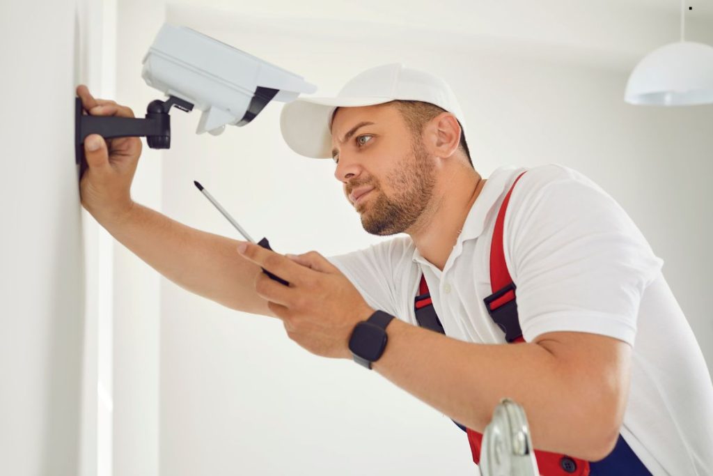 A man in a white shirt and hat repairs a camera for home security installation services.