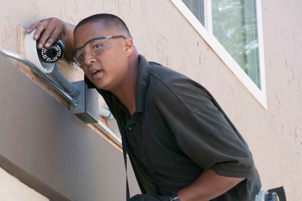 A man wearing glasses adjusts a security camera as part of a home security service installation.