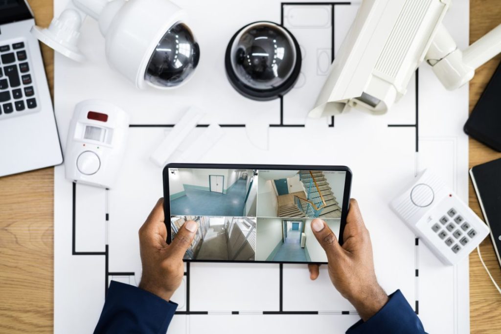 Security camera displayed on a tablet, with a man's hands resting on a wooden table in the background.